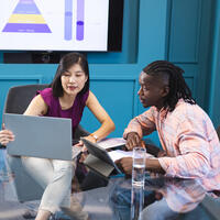 Asian woman and African American man looking at laptop screen together in a modern business office